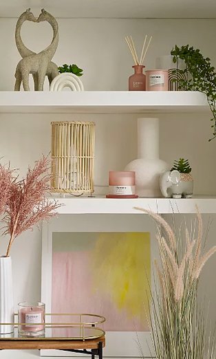 White shelves with giraffe ornament, rainbow artificial plant, elephant artificial plant, pink candle and diffuser set, wicker lamp, pink artificial plant in white vase, green and pink framed print, gold-tone wire tray and pink candle.