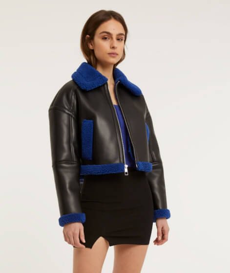 A woman wearing a cropped aviator jacket over a blue top and black mini skirt