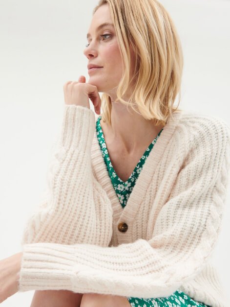 A woman wearing a cream knitted cardigan over a green dress