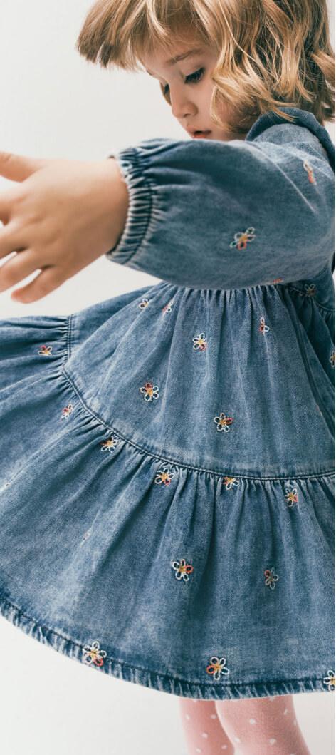A girl twirling in a denim dress with embroidered flowers