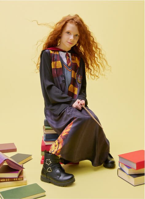 A girl sitting on a pile of books in a Hermione costume