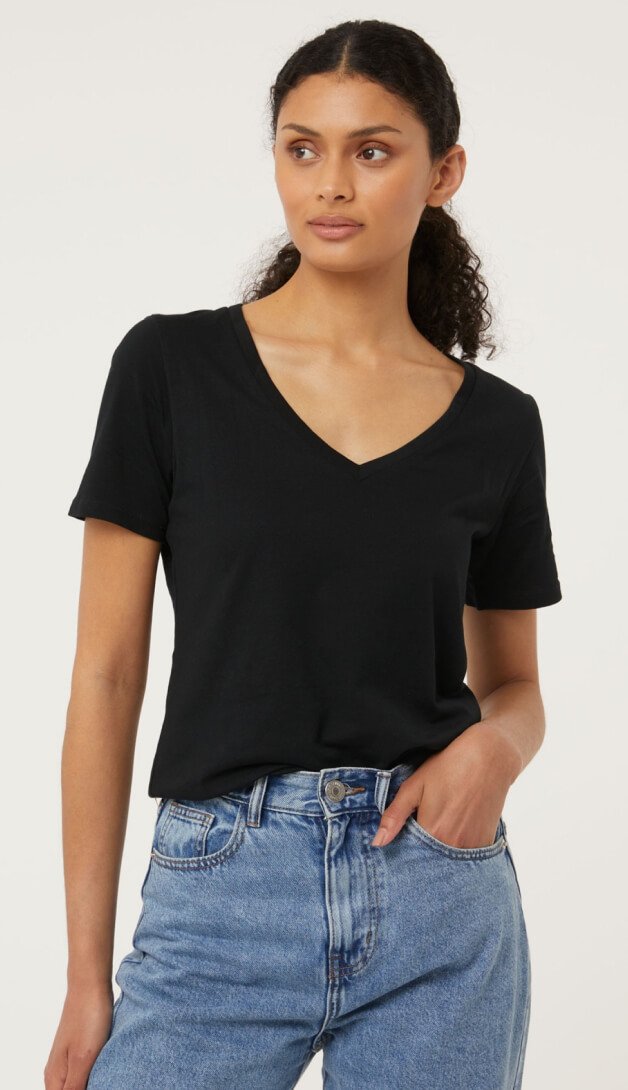A woman posing in a black v neck t-shirt and jeans