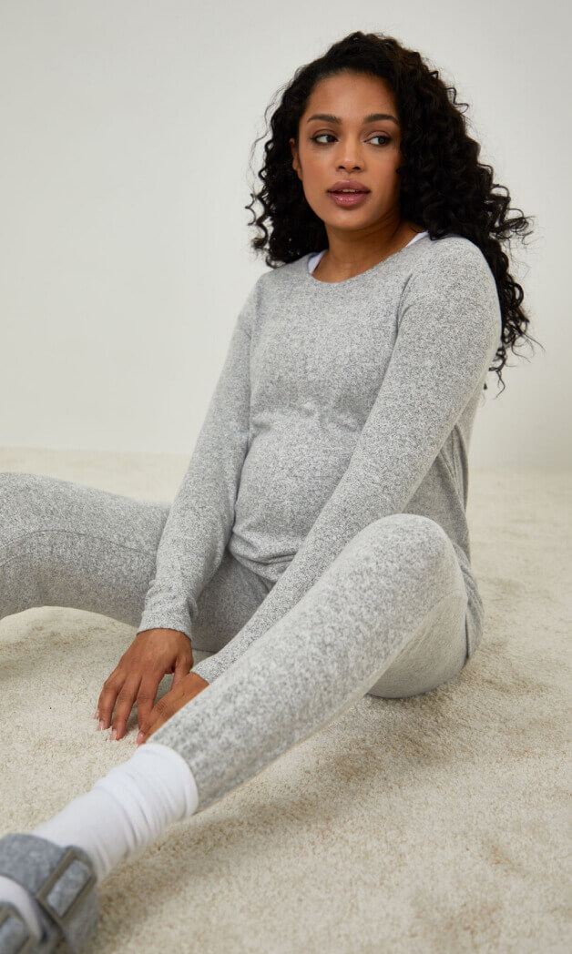 A pregnant woman sitting on the floor in a coordinated joggers and long sleeved top outfit