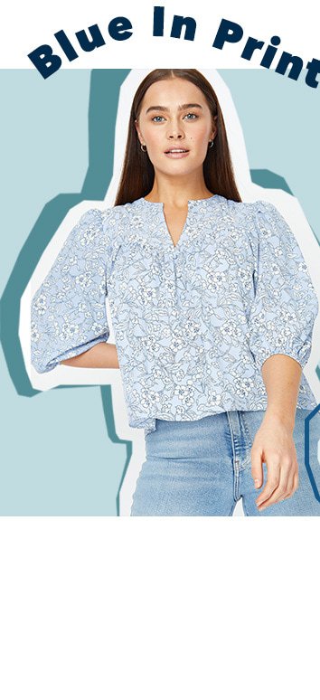 Woman poses wearing blue floral print ruffle trim blouse and blue light wash jeans.