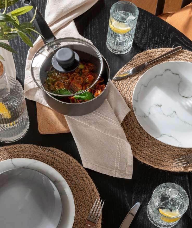 Round table features marble tableware, woven placemats, silver cutlery and ribbed tumblers