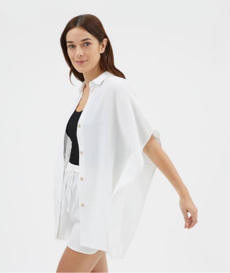 Woman poses wearing white double cloth beach shirt, black vest and white shorts.