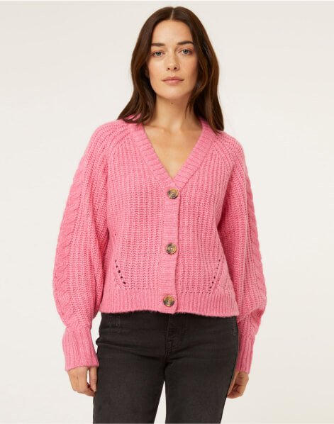 A woman wearing a pink cable knitted cardigan and black jeans