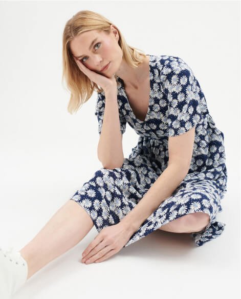 A woman wearing a navy daily print midi dress and white trainers