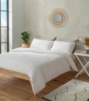 Bedroom setting with rattan mirror, bed with white duvet cover, berber rug.