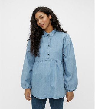 Woman poses smiling wearing maternity blue denim shirt over blue jeans.