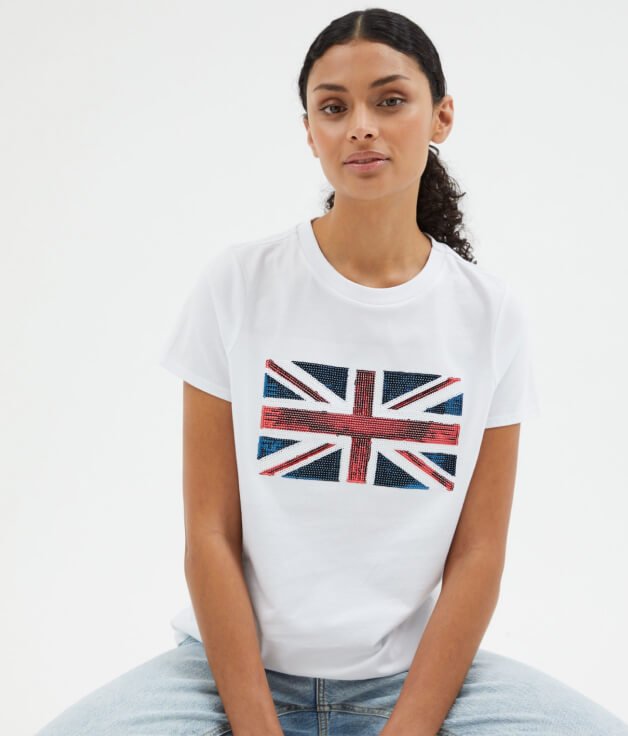 Woman poses wearing matching white sequin Union Jack t-shirt and light blue jeans.