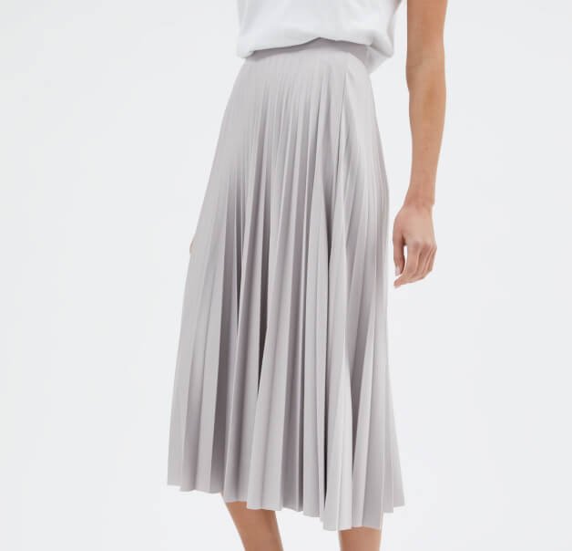 Close-up of woman wearing a white t-shirt tucked into a grey pleated midi skirt.