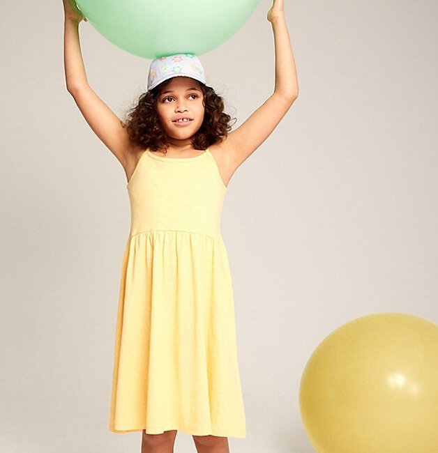 A girl holds ball above her head wearing a light yellow sundress.