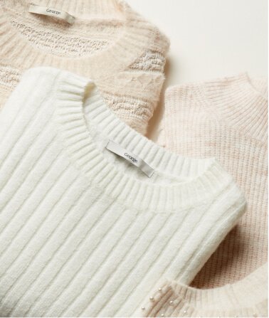 A selection of cream knitted jumpers folded on top of each other.