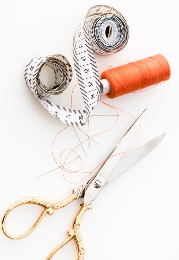 A sewing measuring tape, scissors and orange thread.
