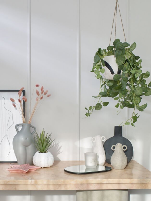 A sidetable topped with a selection of minimalist vases, artificial plants and candles.
