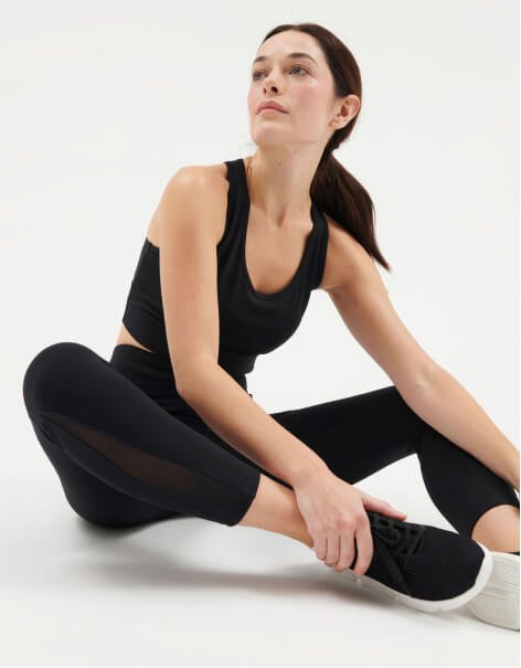 A woman stretching in black sports leggings, a cropped top and trainers.