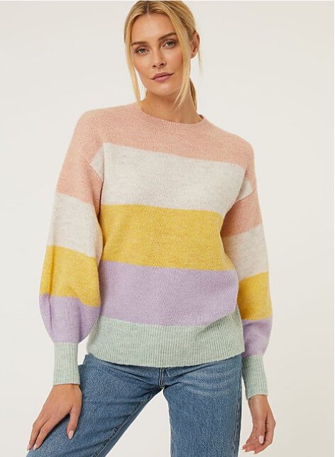 A woman wearing a pastel rainbow striped knitted jumper with jeans.