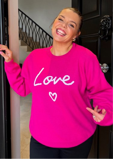 A smiling woman wearing a pink LOVE slogan jumper.