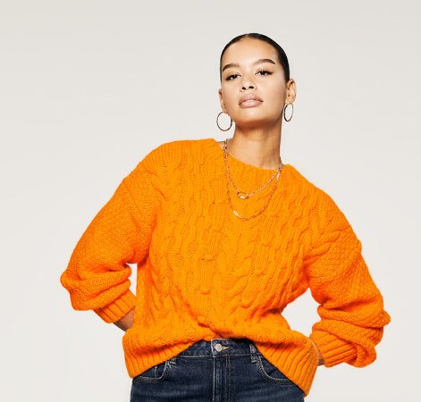 A woman wearing an orange knit jumper and jeans