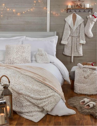 A bedroom decorated with white bedding, white dressing gown and stocking, twinkle lights and other festive decor
