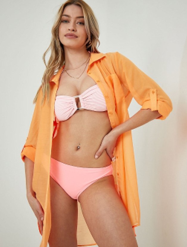 A woman posing in a pink bikini and orange shirt dress cover up. 