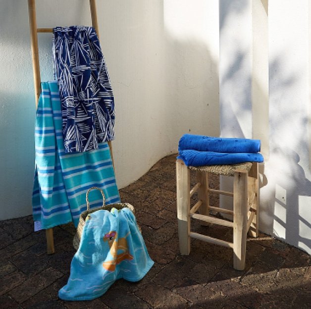 A wooden stool, leaning ladder and woven basket topped with an assortment of blue towels.