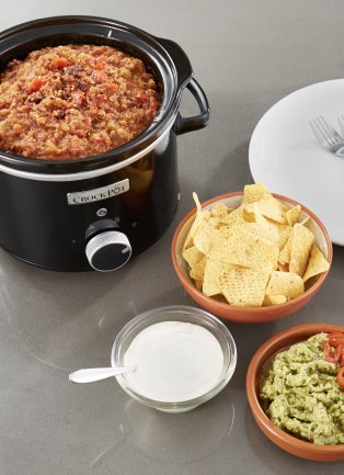 Crock pot meal and side dishes with corn chips and guacamole.