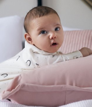 A baby lying on a pillow wearing a white bodysuit.