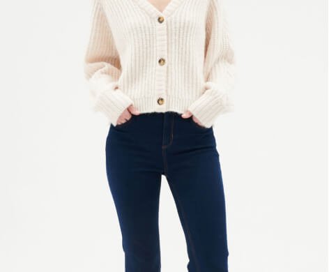 A woman wearing a cream knitted cardigan with dark wash jeans