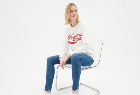 A woman wearing a white Coca-Cola slogan jumper with skinny jeans