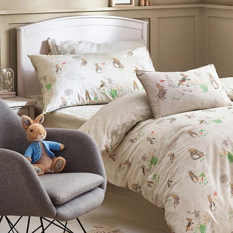 A Peter Rabbit duvet set on a single bed and a Peter Rabbit plush toy on a grey chair