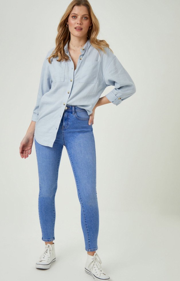 Woman wearing blue button up shirt, jeans and white trainers.