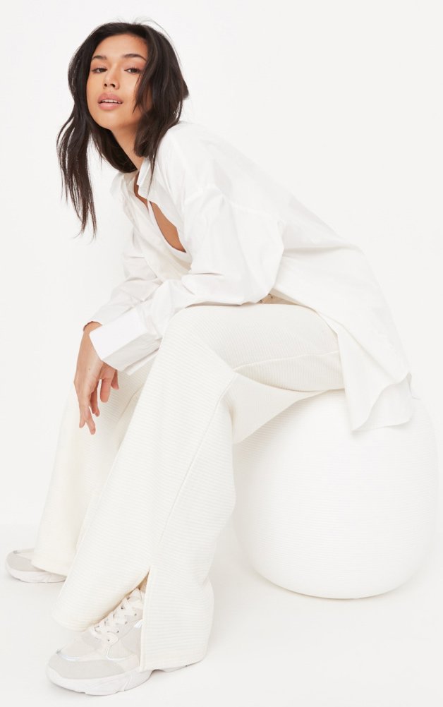 Woman wearing white button up shirt and white trousers with trainers.