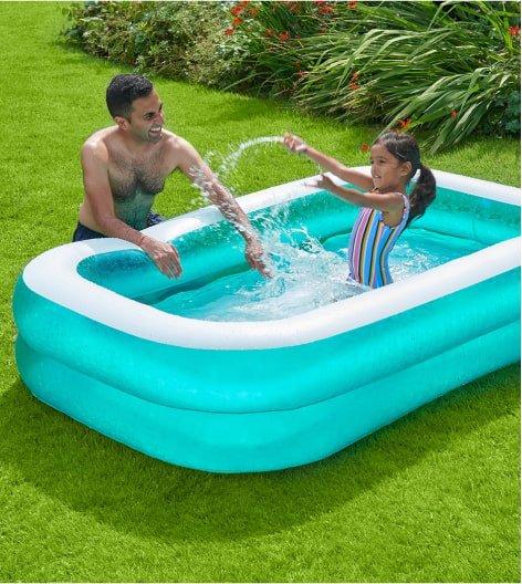 Family playing in paddling pool in garden.