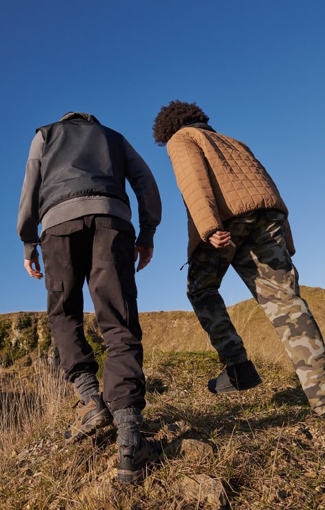 A dad and his child hiking in black, brown and camo-print hiking gear.