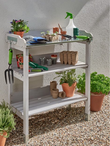 A white garden table topped with various plants, pots and gardening tools.
