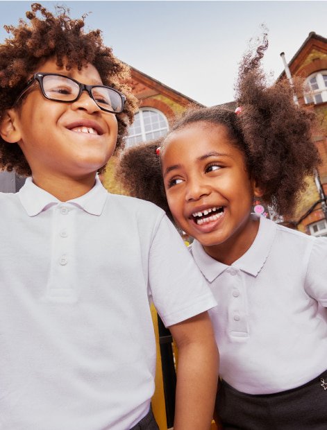 Two laughing school kids wearing white polo shirts.