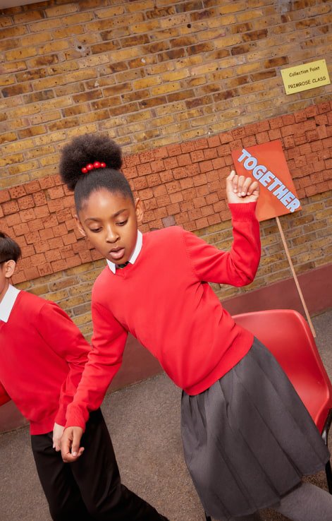 A school girl wearing a red school jumper, white shirt and grey skirt.