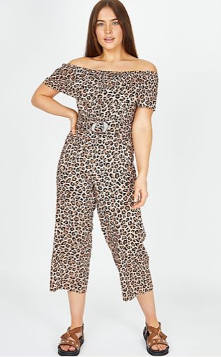 Woman poses with hand on hip wearing leopard print belted Bardot jumpsuit and brown studded sandals.