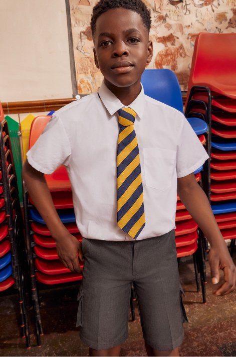 A boy wearing a white shirt, yellow and navy striped tie and grey school shorts.