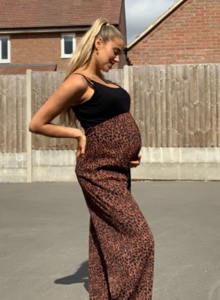 Pregnant woman poses side-on outiside wearing laopard print maxi dress.
