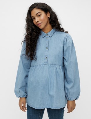 Woman poses wearing light blue denim shirt and jeans.