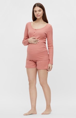Pregnant woman poses with hand on bump wearing pink long-sleeved top and shorts pyjama set.