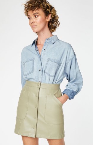 Woman wearing denim button up shirt and green faux leather button up skirt.