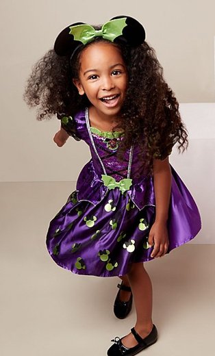 Girl poses wearing Disney Minnie Mouse purple witch fancy dress costume with white boxes in the background