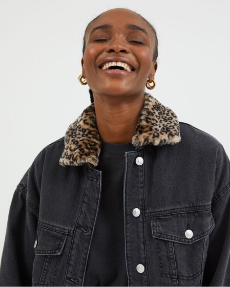 Woman wearing grey denim jacket with faux fur collar.