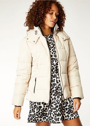 Woman poses wearing cream padded hooded coat over leopard print mini dress.