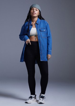 Woman poses wearing black jeggings, cream ribbed crop top, blue oversized shacket, grey hat and black and white trainers.